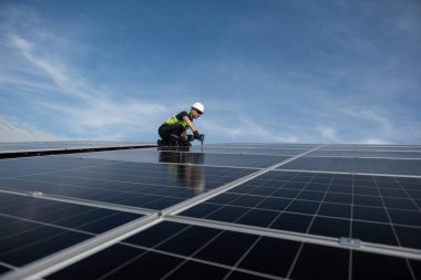 Teknisyen yeşil enerji için fabrikanın çatısına güneş panelleri kuruyor. Güvenlik teçhizatı konusunda yetenekli bir teknisyen çatıdaki bir güneş paneli tesisi üzerinde çalışıyor. Temiz enerji yenilenebilir enerji teknolojisi.