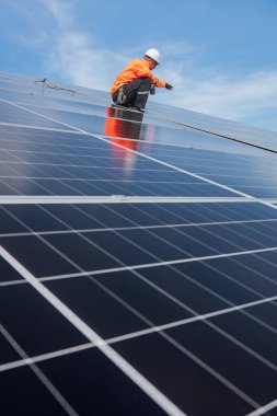 Teknisyen yeşil enerji için fabrikanın çatısına güneş panelleri kuruyor. Güvenlik teçhizatı konusunda yetenekli bir teknisyen çatıdaki bir güneş paneli tesisi üzerinde çalışıyor. Temiz enerji yenilenebilir enerji teknolojisi.
