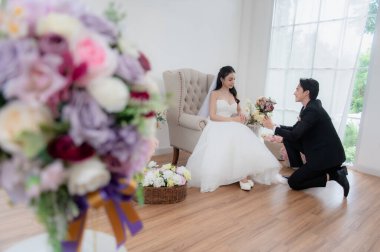 Gelin ve Damat, Düğün Töreninden Önce Evde Romantik Bir Anı Paylaşıyorlar. Siyah smokin giymiş ve elinde buket tutan yakışıklı damat..