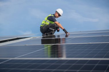 Teknisyen yeşil enerji için fabrikanın çatısına güneş panelleri kuruyor. Güvenlik teçhizatı konusunda yetenekli bir teknisyen çatıdaki bir güneş paneli tesisi üzerinde çalışıyor. Temiz enerji yenilenebilir enerji teknolojisi.