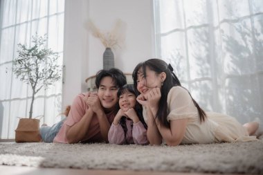 Mutlu Asyalı bir aile yerde uzanıyor ve evde birlikte gülümsüyor, ebeveynler ve kızlar kaliteli vakit geçiriyorlar. Aile mutluluğu, bağlılık, ebeveynlik ve neşeli ev hayatı kavramı.