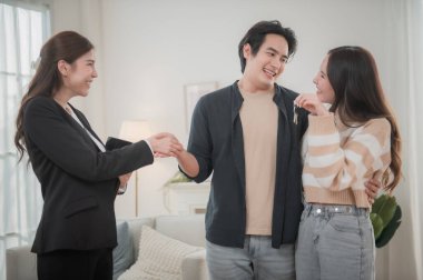 Mutlu Asyalı aile genç çiftimiz yeni ev almak için gayrimenkul alırken anahtarlarını tutuyorlar. İş finansmanı, finansal planlama için banka mevduatı.