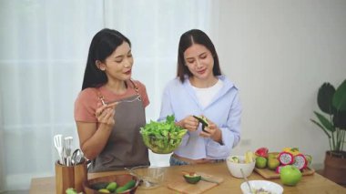 Önlük takan genç bir Asyalı kadın evde mutfakta sağlıklı malzemeler ve sebzelerle durup arkadaşlarıyla tatilde yemek için taze ev yapımı salata yapıyor. Sağlıklı konsept.