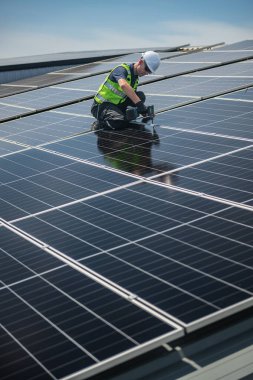 Teknisyen yeşil enerji için fabrikanın çatısına güneş panelleri kuruyor. Güvenlik teçhizatı konusunda yetenekli bir teknisyen çatıdaki bir güneş paneli tesisi üzerinde çalışıyor. Temiz enerji yenilenebilir enerji teknolojisi.