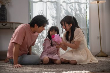 Asyalı bir aile çocuğuna evde para biriktirmeyi öğretiyor. Ailesi ve kızı domuz kumbarasına bozuk para koyuyor. Finansal eğitim, aile bağı, ebeveynlik, tasarruf ve çocukluktan kalma akıllı para alışkanlıkları.