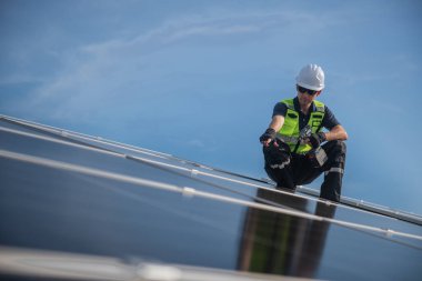 Teknisyen yeşil enerji için fabrikanın çatısına güneş panelleri kuruyor. Güvenlik teçhizatı konusunda yetenekli bir teknisyen çatıdaki bir güneş paneli tesisi üzerinde çalışıyor. Temiz enerji yenilenebilir enerji teknolojisi.