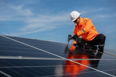 Teknisyen yeşil enerji için fabrikanın çatısına güneş panelleri kuruyor. Güvenlik teçhizatı konusunda yetenekli bir teknisyen çatıdaki bir güneş paneli tesisi üzerinde çalışıyor. Temiz enerji yenilenebilir enerji teknolojisi.