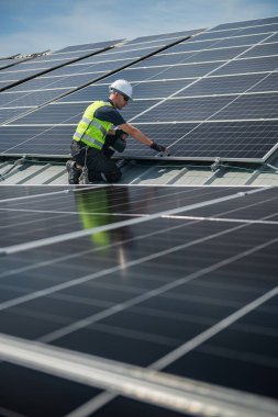 Teknisyen yeşil enerji için fabrikanın çatısına güneş panelleri kuruyor. Güvenlik teçhizatı konusunda yetenekli bir teknisyen çatıdaki bir güneş paneli tesisi üzerinde çalışıyor. Temiz enerji yenilenebilir enerji teknolojisi.