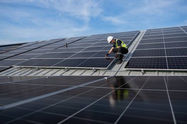 Teknisyen yeşil enerji için fabrikanın çatısına güneş panelleri kuruyor. Güvenlik teçhizatı konusunda yetenekli bir teknisyen çatıdaki bir güneş paneli tesisi üzerinde çalışıyor. Temiz enerji yenilenebilir enerji teknolojisi.