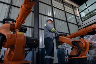 Robotik kol ve işletim makinesinin yanında duran miğfer güvenlikli mühendis. Teknisyen, tamir onarım elektronik işlemleri için kontrol ediyor..