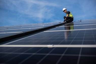 Teknisyen yeşil enerji için fabrikanın çatısına güneş panelleri kuruyor. Güvenlik teçhizatı konusunda yetenekli bir teknisyen çatıdaki bir güneş paneli tesisi üzerinde çalışıyor. Temiz enerji yenilenebilir enerji teknolojisi.
