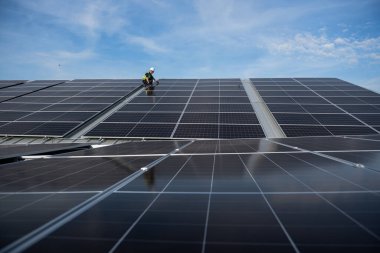 Teknisyen yeşil enerji için fabrikanın çatısına güneş panelleri kuruyor. Güvenlik teçhizatı konusunda yetenekli bir teknisyen çatıdaki bir güneş paneli tesisi üzerinde çalışıyor. Temiz enerji yenilenebilir enerji teknolojisi.