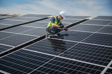Teknisyen yeşil enerji için fabrikanın çatısına güneş panelleri kuruyor. Güvenlik teçhizatı konusunda yetenekli bir teknisyen çatıdaki bir güneş paneli tesisi üzerinde çalışıyor. Temiz enerji yenilenebilir enerji teknolojisi.