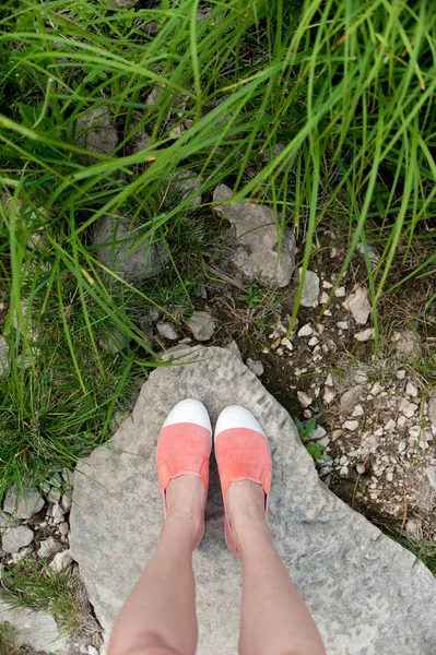 Overhead photo of feet on a background of big stone and grass. Women feets view from above. Exploring, travelling, tourism, leisure.