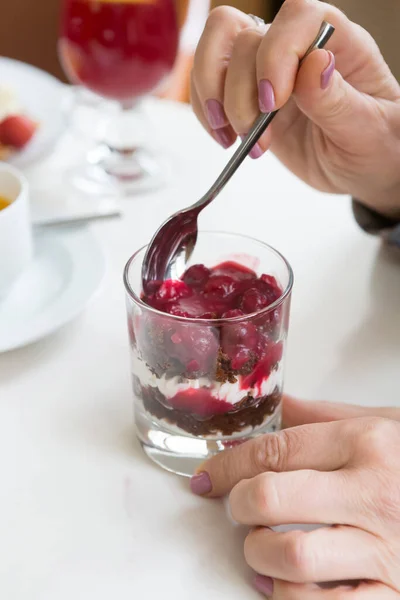 Woman hands with spoon over glass of granola with cream and berries
