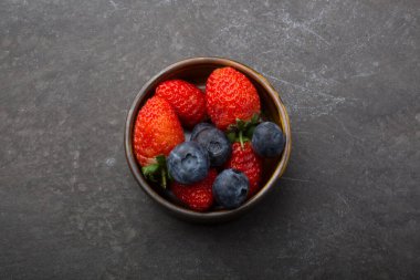 Siyah arka planda küçük bir fincanda çilek ve yaban mersini.