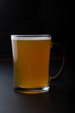 Siyah arka planda servis edilen bir bardak bira.