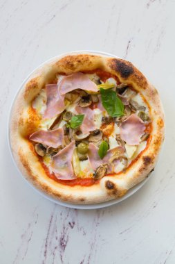 Kafe masasında jambon ve mantarlı yuvarlak Napoli pizzası.