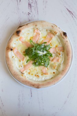 Üstünde roka ve peynir olan somon balıklı pizza.