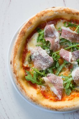 Üstünde roka ve peynir olan Napoli usulü jambonlu pizza.