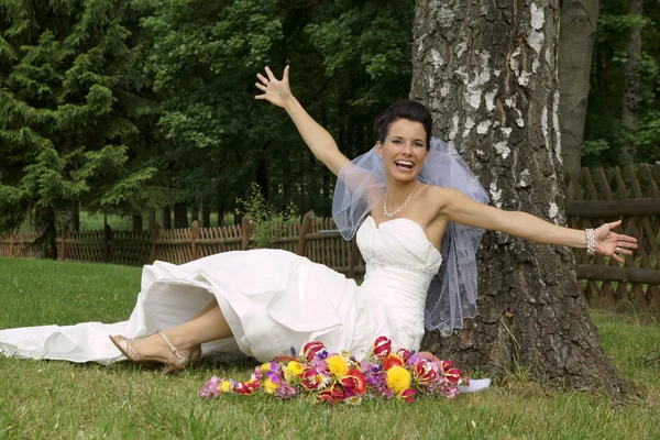 Smiling bride sitting under tree — Stock Photo, Image