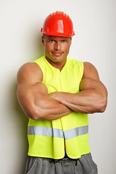 Muskulöser Arbeiter mit Helm und Arbeitsweste — Stockfoto