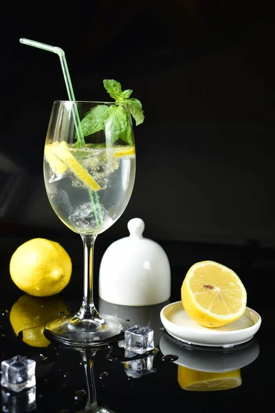 Drink with lemon, mint and ice in a glass on a black glossy background