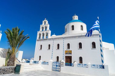 Yunanistan 'ın Oia kentindeki Ortodoks kilisesi, Yunan bayrağıyla dolu bir yaz gününde. Güzel berrak mavi gökyüzü.