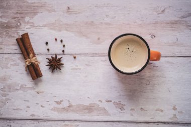 Beyaz ahşap arka planda tarçın ve yıldız anason kaplı klasik turuncu kahve fincanının üst görüntüsü. Noel baharatları.