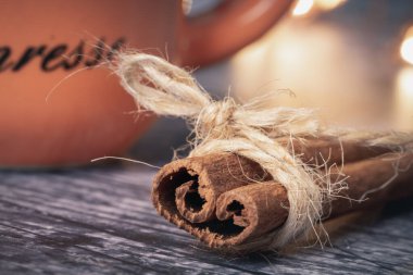 Bir ipin sarılı olduğu tarçın çubuğunun yakın çekimi. Arka planda turuncu bardak ve bokeh ışığı var. tatil kavramı