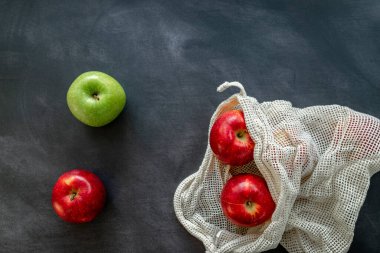 Kırmızı ve yeşil elmalar, koyu bir arka planda pamuk örgü eko torbasında. Sürdürülebilirlik ve sıfır atık alışveriş konsepti. Üst görünüm