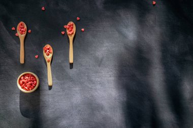 Üç tahta kaşık ve koyu arkaplanda kırmızı kalp şeklinde şeker dolu bir kase. Üst Manzara. metin için kopyalama alanı olan panoramik biçim