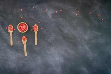 Üç tahta kaşık ve koyu arkaplanda kırmızı kalp şeklinde şeker dolu bir kase. Üst Manzara. metin için kopyalama alanı olan panoramik biçim