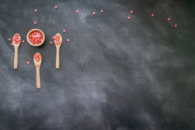 Üç tahta kaşık ve koyu arkaplanda kırmızı kalp şeklinde şeker dolu bir kase. Üst Manzara. metin için kopyalama alanı olan panoramik biçim