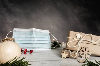 Noel ve sıfır atık, çevre dostu ambalaj. El işi kağıdına sarılmış hediyeler ve ahşap bir masada Noel süsü. Gri arka planda mavi cerrahi maske. Ekolojik Noel tatili konsepti, ekolojik dekor