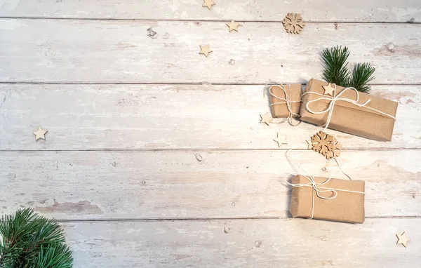 Christmas and zero waste, eco friendly packaging. wrapped gifts in craft paper with wooden snowflakes and pine branch on a wooden table. ecological Christmas holiday concept, eco decor. Top view