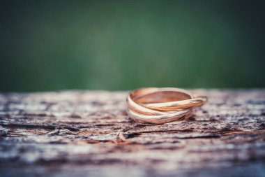 Ahşap zemin üzerinde üç halka olan bir yüzüğün yakın çekimi. Altın, beyaz altın ve gül sarısı düğün mücevherleri. seçici odak ile makro çekim ve metin için boşluk kopyala