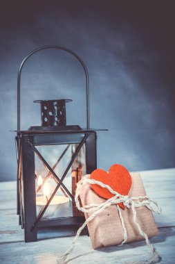 Kırmızı bir kalbi olan el yapımı bir hediye. Arka planda yanan bir fener var. Çevre dostu kavram