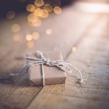 Tahta bir masaya el işi kağıtla sarılmış bir hediye. Arka planda güzel bir bokeh ışığı var. Çevre dostu kavram