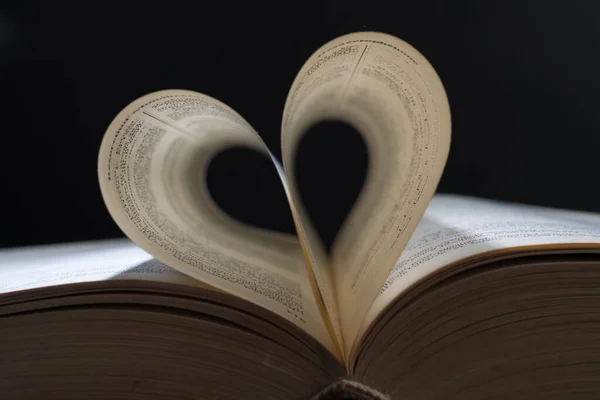 Close up heart shape from paper book on dark background. lights and shadows concept.