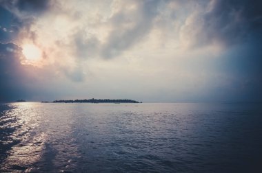 Fırtınalı bir günde, gün batımında palmiye ağaçları olan tropik bir ada..