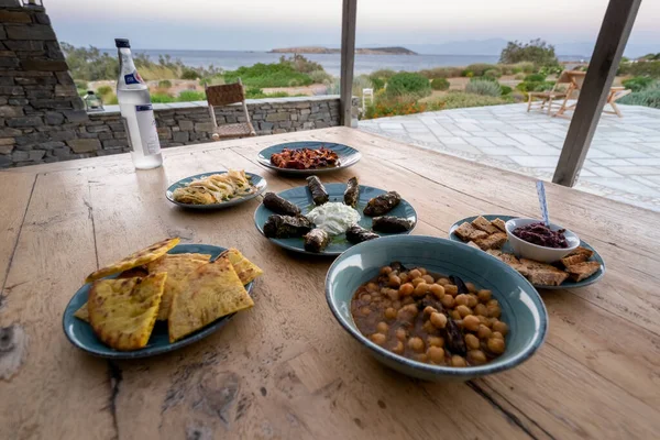 Greek food. pita, tzatziki, stuffed vine leaf, chickpeas salad and vegetables, ouzo bottle. Traditional different greek dishes set. Food for share. Close-up. mediterranean sea in the background