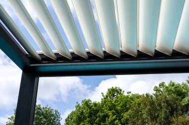 Trendy outdoor patio pergola. sky and clouds pass through the metallic structure. green trees in the background