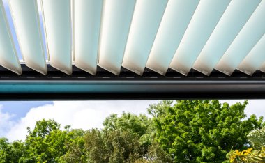Trendy outdoor patio pergola. sky and clouds pass through the metallic structure. green trees in the background