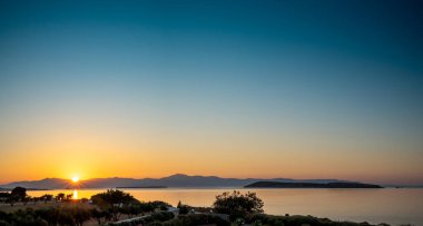 Watching a golden sunset with the sun hiding behind far away rocks of Naxos into the sea from Drios, Paros island Greece.