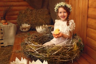 Bir yuvada oturan kızıl saçlı kız kollarında tavuk tutuyor.