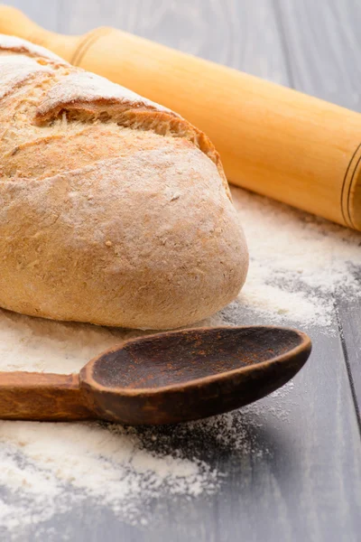 Una pagnotta di pane, farina con un cucchiaio e un mattarello — Foto Stock