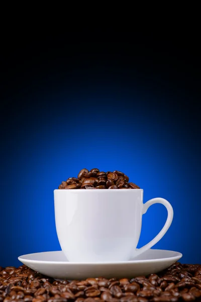 咖啡豆在蓝色背景上的白色杯子 免版税图库图片