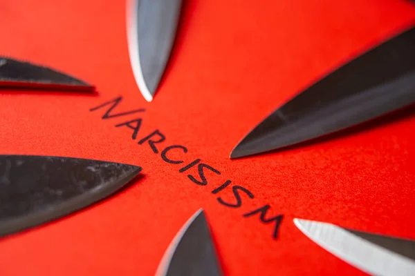 Written Narcisism in black on red paper, with knife blades next to it