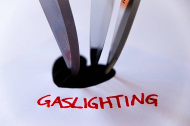 Sözcük Gaslighting, beyaz kağıda kırmızı ile yazılmış, siyah kalp tasarımının yanında, bıçaklı.